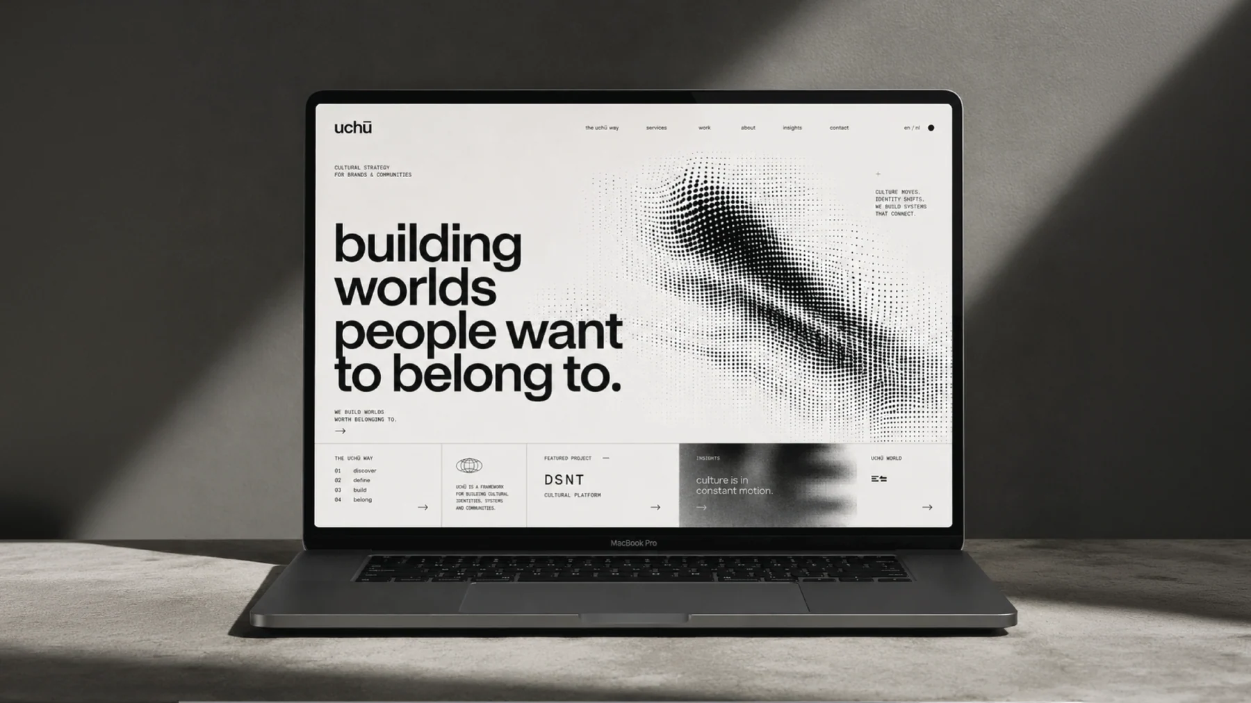 De homepage van The Uchu Way op een laptop, hard strijklicht en slagschaduw op een betonnen tafel